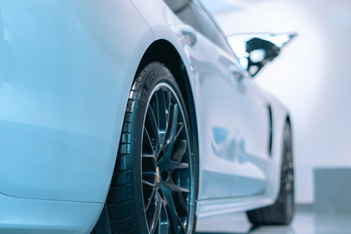 Close-up of a white car's front wheel and headlight in a showroom setting.